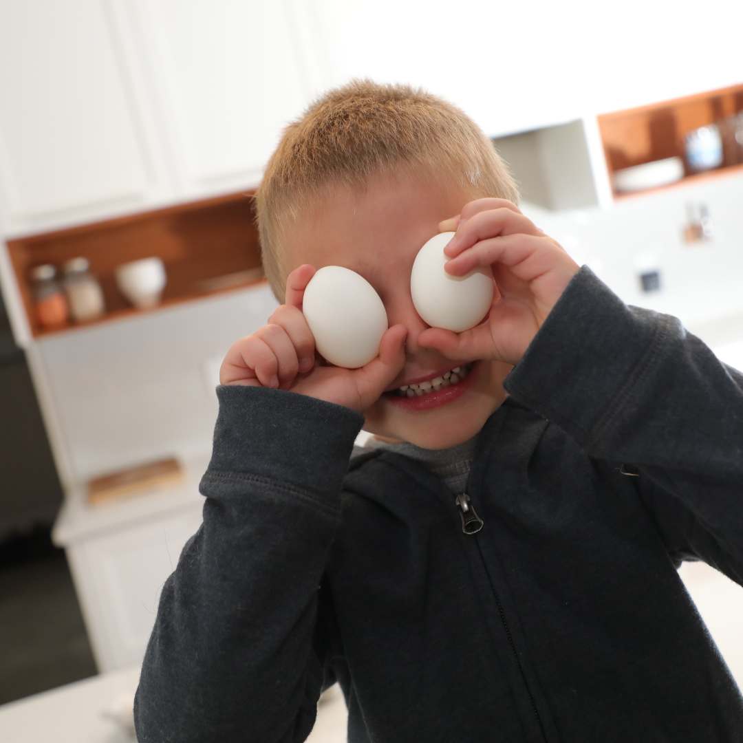 Child holding two eggs over eyes in kitchen