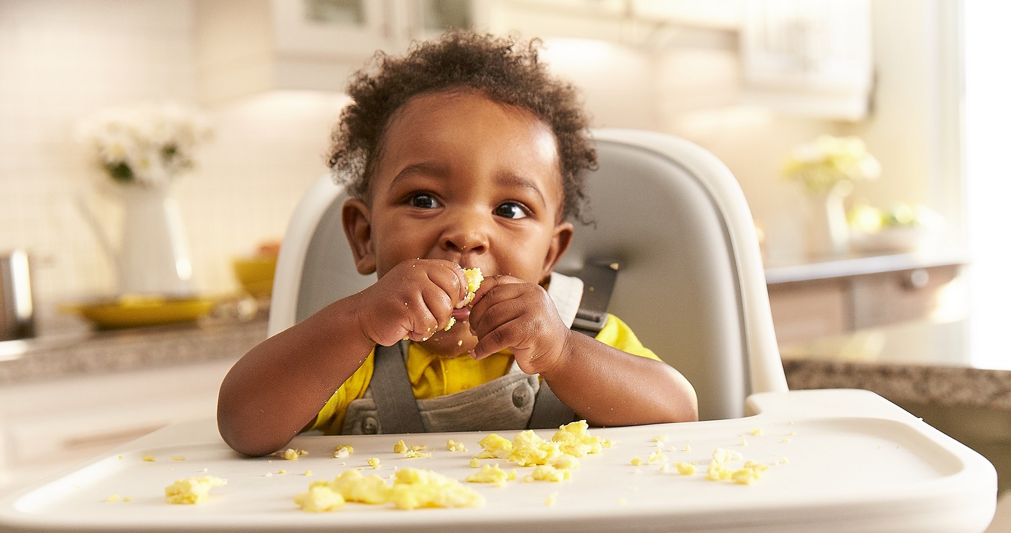 Baby eating in high chair with food scattered