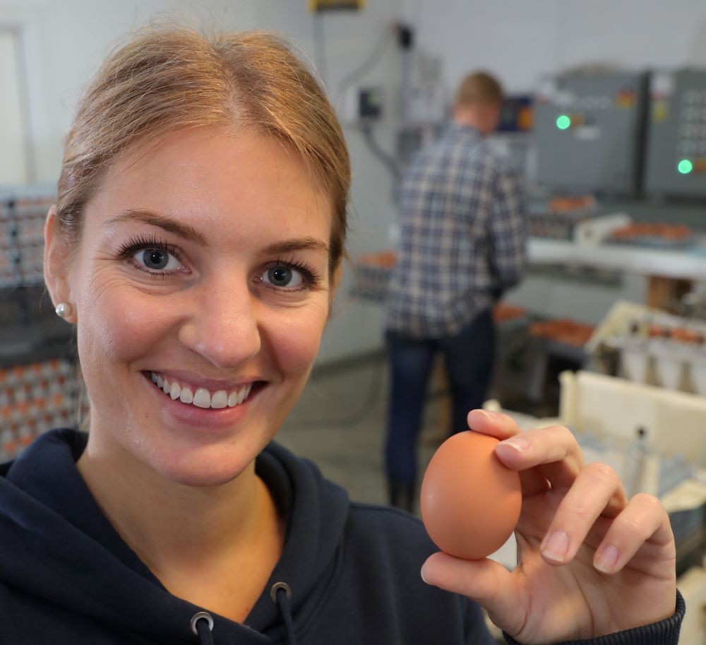 Woman holding egg in front of egg packaging facility.