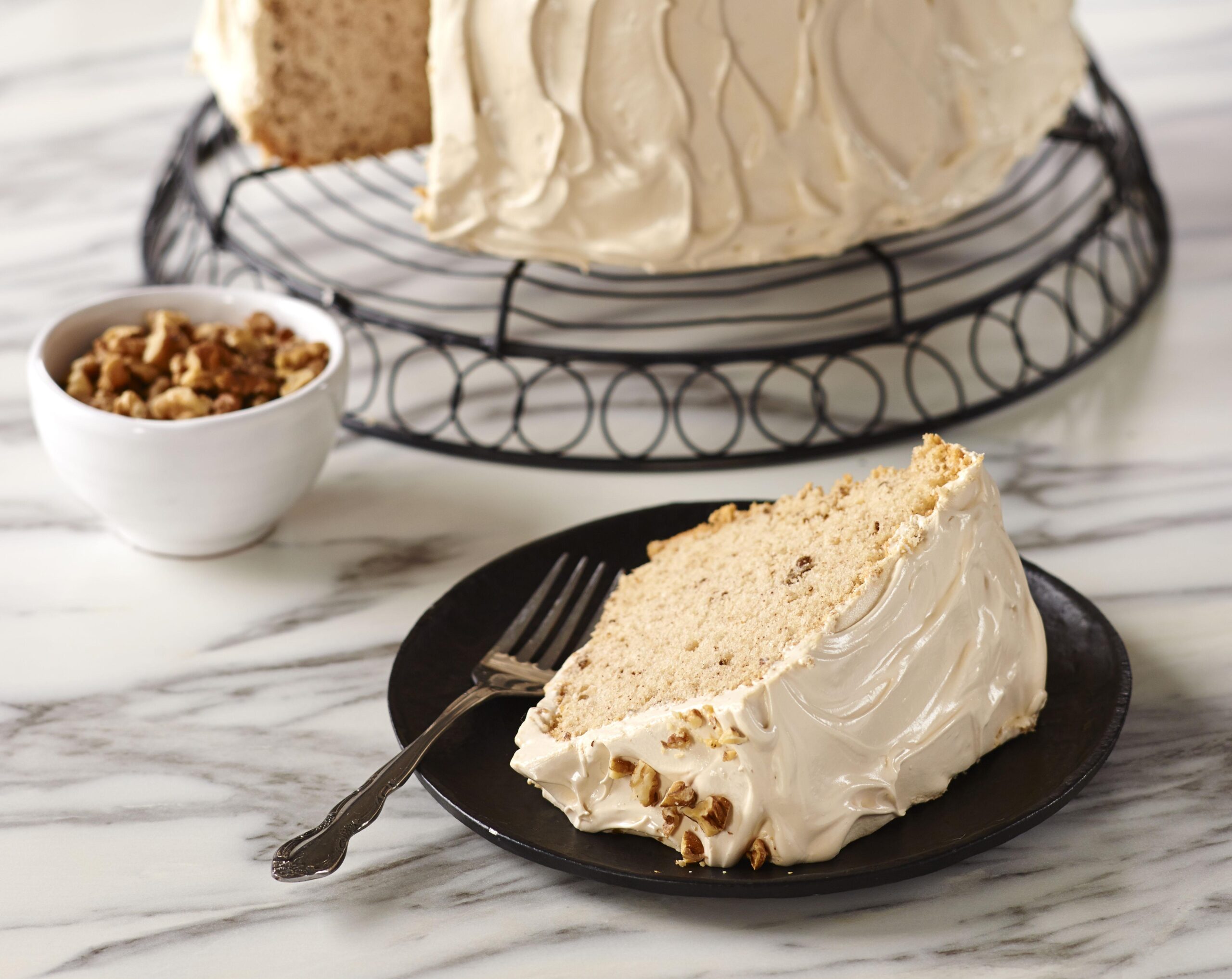 Slice of frosted walnut cake on black plate