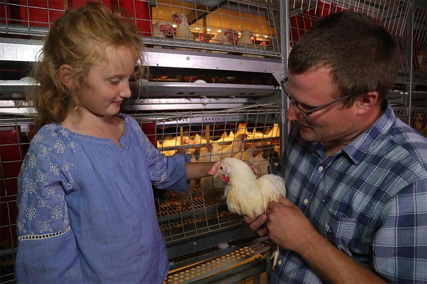 Man showing young girl a white chicken indoors.